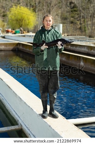 Portrait of successful female owner of sturgeon farm showing freshly caught fish outdoors..