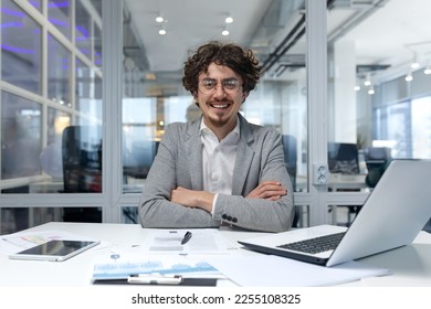 Portrait of successful financier businessman, hispanic man sitting at workplace working with documents and laptop inside office, man with crossed arms smiling and looking at camera. - Shutterstock ID 2255108325