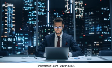 Portrait of a Successful Handsome Businessman Working on Laptop Computer in Big City Office Late in the Evening. Finance Investment Analyst Checking Line and Pie Graphs from Project Management Report.