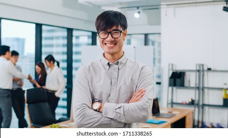 Portrait Of Successful Handsome Executive Businessman Smart Casual Wear Looking At Camera And Smiling, Arms Crossed In Modern Office Workplace. Young Asia Guy Standing In Contemporary Meeting Room.