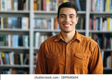 Portrait Of Successful Hispanic Business Man Looks Directly At The Camera, Smile. Happy Male Freelancer Or Student Standing In Modern Office Or University Library