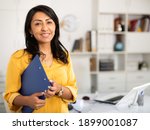 Portrait of successful Hispanic business woman with folder of documents in her hands, standing in modern office