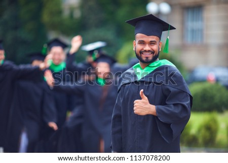 portrait of successful indian student in graduation gown thumb up