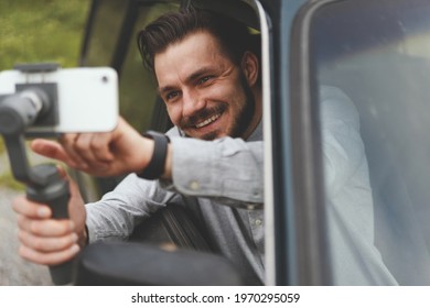 Portrait Of Successful Man Recording Video At Phone With Steadycam. Smiling Man Sitting At The Passenger Seat Of Black Car Holding Steadycam While Recording Steaming Video Sharing Traveling Experience