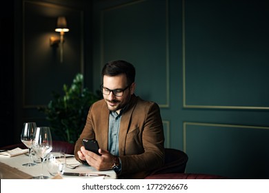 Portrait Of A Successful Man At The Table In Luxurious Restaurant, Using Smart Phone.