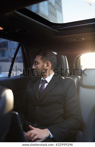Portrait of successful\
Middle-Eastern businessman looking out of window of expensive\
luxury car