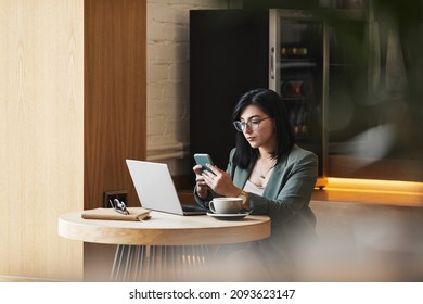 Portrait of successful Middle-Eastern businesswoman using smartphone in cafe while working remotely in elegant wooden interior, copy space