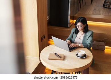 Portrait of successful Middle-Eastern woman using laptop in cafe while working remotely in elegant wooden interior, copy space - Powered by Shutterstock