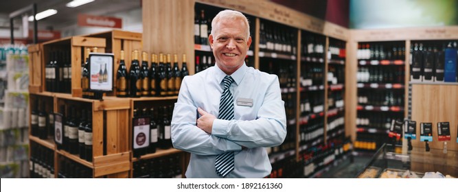 Portrait of a successful owner of a wine store. Senior businessman standing in wine store with his arms crossed and smiling at camera. - Powered by Shutterstock