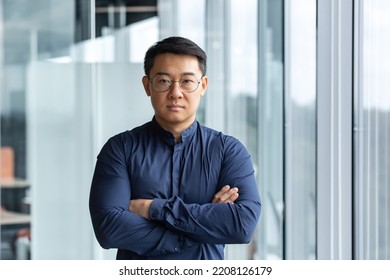 Portrait Of Successful And Serious Asian Boss In Shirt, Man Looking At Camera With Crossed Arms Inside Modern Office Building Near Window