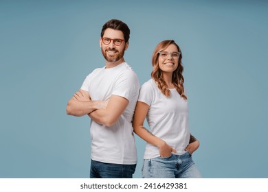 Portrait of successful smiling man and woman wearing white t shirt and stylish glasses isolated on blue background. Happy attractive fashion models with arms crossed posing for pictures in studio - Powered by Shutterstock