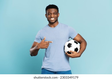 Portrait of successful sports man, African American soccer player holding ball looking at camera isolated on blue background. Sport, competition, healthy lifestyle concept - Powered by Shutterstock