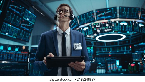 Portrait of a Successful Stock Exchange Manager Wearing Headphones, Working in Modern Office. Proactive Trader Browsing Internet on a Tablet Computer, Using Software with Stock Market Auctions - Powered by Shutterstock