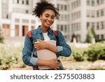 Portrait Of Successful Student. Happy African American Teenager Girl Posing Holding Books Smiling Looking At Camera Standing Near Modern University Building Outside. Studentship, Modern Education