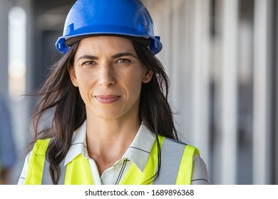 Portrait of successful woman constructor wearing helmet and safety yellow vest. Portrait of architect standing at building site and looking at camera with copy space. Mature successful woman engineer.