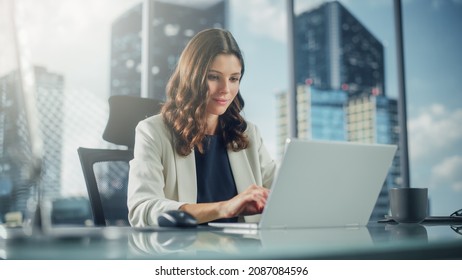 Portrait of Successful Young Businesswoman Sitting at Her Desk Working on Laptop Computer in Big City Office. Confident Professional CEO Managing Environmental, Social and Corporate Governance