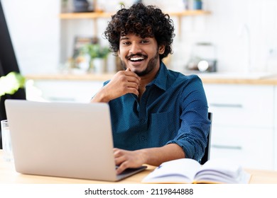 Portrait of a successful young Indian male freelance using laptop and looks at the camera, remote work from home, online education