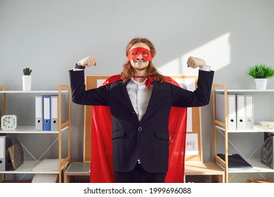 Portrait Of Superhero Business Man Or Employee. Funny Energetic Worker In Red Super Hero Mask And Cape Standing In Office, Smiling And Flexing Arms. Commitment To Work And Can-do Attitude Concept