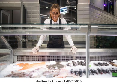 Portrait of supermarket deli worker working in fish department. Frozen fish on the ice ready for sale.