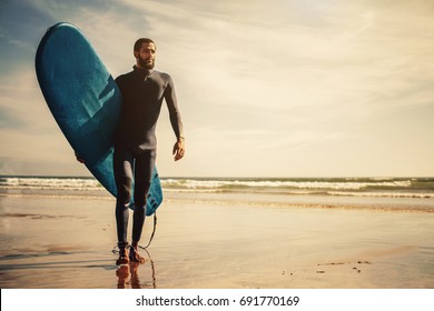 Portrait Of Surfer Man With Surf Board On The Beach. Mixed Race Black Skin And Beard. Summer Sport Activity 