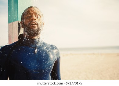 Portrait surfer man taking a shower on the beach. Mixed race black skin and beard. Summer sport activity 