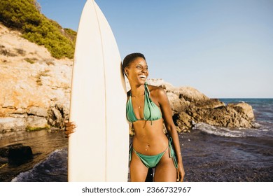 Portrait of a surfer standing on the beach in swimwear, with her surfboard by her side. Happy woman doing beach activities during summer vacation. - Powered by Shutterstock