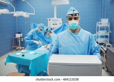 Portrait of surgeon holding ice box while colleagues performing operation in operation room. Healthcare workers in the Coronavirus Covid19 pandemic
 - Powered by Shutterstock