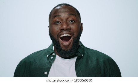 Portrait Of Surprised African Guy Covering Mouth With Hands In Studio. Closeup Happy Male Face Smiling At Camera. Joyful Afro Man With Open Mouth Posing On Grey Background.