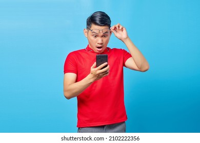 Portrait of surprised asian young man holding glasses and reading incoming message on smartphone isolated on blue background - Powered by Shutterstock