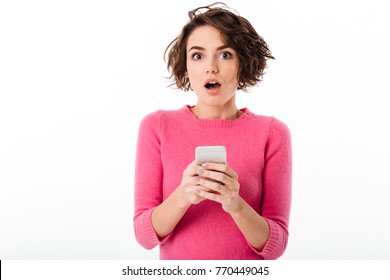 Portrait Of A Surprised Attractive Girl Holding Mobile Phone And Looking At Camera Isolated Over White Background