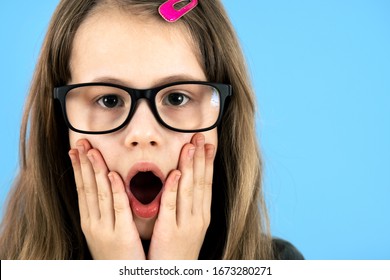 Portrait Of Surprised Child Girl Wearing Looking Glasses Holding Hands To Her Face Isolated On Blue Background.