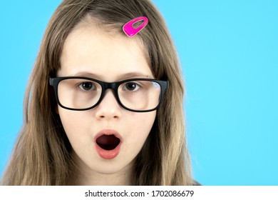 Portrait Of Surprised Child Girl Wearing Looking Glasses Isolated On Blue Background.