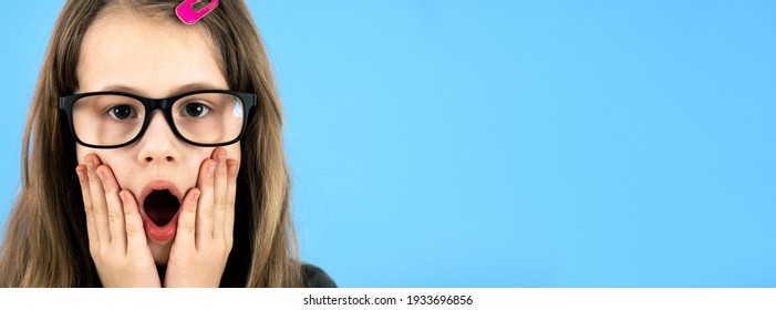 Portrait Of Surprised Child Girl Wearing Looking Glasses Holding Hands To Her Face Isolated On Blue Background.