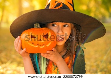 Portrait of a surprised child in a witch costume with a carved pumpkin in his hands. Preparing for the holidays. Autumn seasonal amazing discounts before Halloween