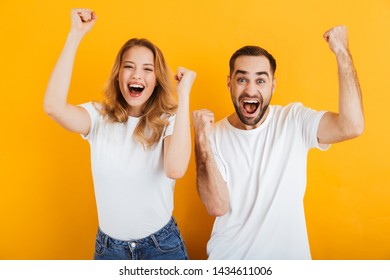 Portrait of surprised content couple man and woman in basic t-shirts rejoicing and clenching fists isolated over yellow background - Shutterstock ID 1434611006