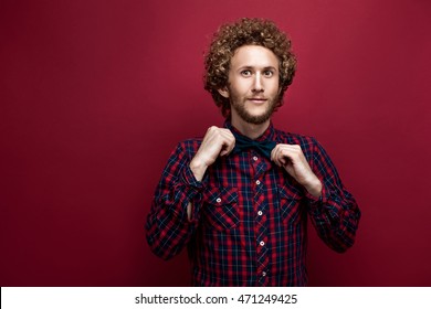 Portrait of surprised curly-haired man in checked shirt and bow-tie on red background. Isolate - Powered by Shutterstock