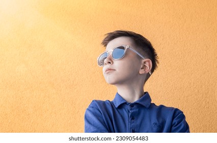 Portrait of a surprised cute boy in sunglasses. A child with an important face is isolated on an orange background. Looking to the side, space for text - Shutterstock ID 2309054483