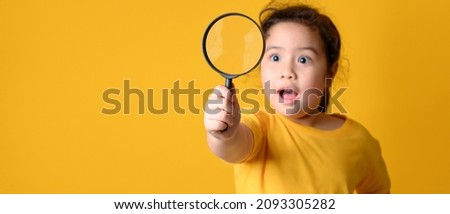 Portrait of surprised cute  little asian girl looking through a magnifying glass. Education concept.