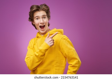 Portrait of a surprised, excited  teenage boy in bright yellow hoodie pointing his index finger away. Purple background with copy space. Adolescents and lifestyle. Youth fashion.  - Shutterstock ID 2154763141
