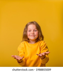 Portrait Of Surprised Funny Little Kindergarten Or School Girl Isolated Over Yellow Background. Open Hands. Stylish Child With Open Palm And Finger Pointed Up. Promoting School Supplies.