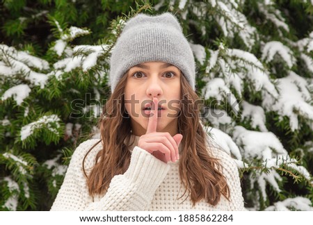 Portrait of a surprised girl against the background of a tree, who asks to be quiet. Portrait of a surprised girl against the background of a tree, who wants to tell a secret.