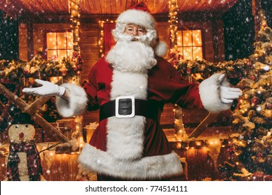Portrait of surprised Santa Claus in the courtyard of his house decorated with Christmas lights. Christmas and New Year concept.
