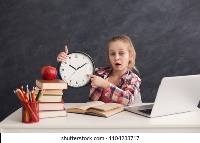 Portrait Of Surprised Smart Girl Sitting With Stack Of Books And Laptop, Holding Big Clock And Pointing On It. Education, Development, Time Management, Deadline, Time To Study, School Concept