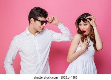 Portrait Of A Surprised Smartly Dressed Couple Posing While Looking At Each Other Isolated Over Pink Background