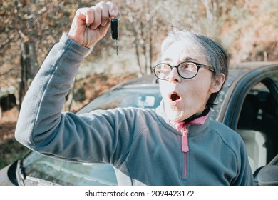 Portrait Of A Surprised Smiling Senior Woman Learning To Drive Car Holding The Car Key To Camera.Safety Drive.Learning New Hobby,habit And Skill For This New Year.Old Person Approving Driving License