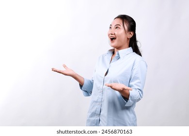 Portrait of surprised smiling young pretty Asian woman looking upward and presenting with open palms gesture in isolated studio white background - Powered by Shutterstock