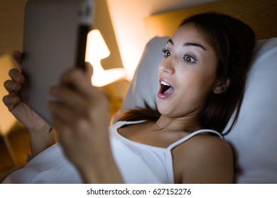 Portrait Of Surprised Woman Looking Her Digital Tablet In The Bed At Night.