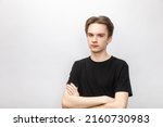 Portrait of suspicious young man wearing black tshirt holding his hands crossed looking at camera. Studio shot on gray background