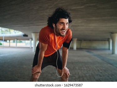 Portrait of sweaty and tired young male fit person taking a break after jogging in city street under the bridge - Powered by Shutterstock