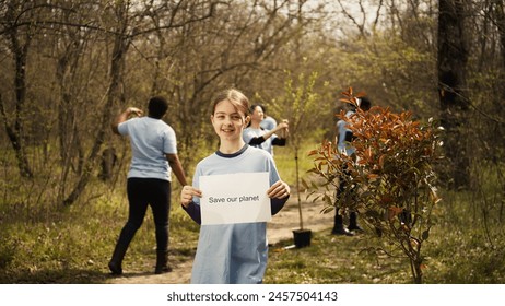 Portrait of sweet girl with save our planet poster against pollution and illegal dumping, volunteering to restore and preserve nature in the forest. Little child shows awareness sign. Camera B. - Powered by Shutterstock - Get 15% off with code: PIKWIZARD15